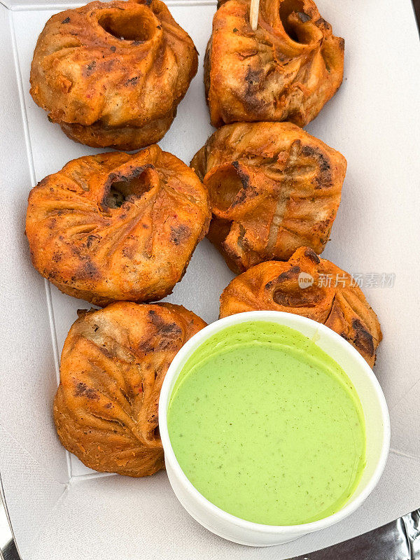 特写图片:纸板箱里装着6个鸡肉tikka momos，两排鸡肉馅饺子，一碗一次性的薄荷和香菜酸辣酱，高架视图